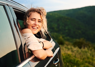 joven sonriente asomada de coche con fondo de campo verde