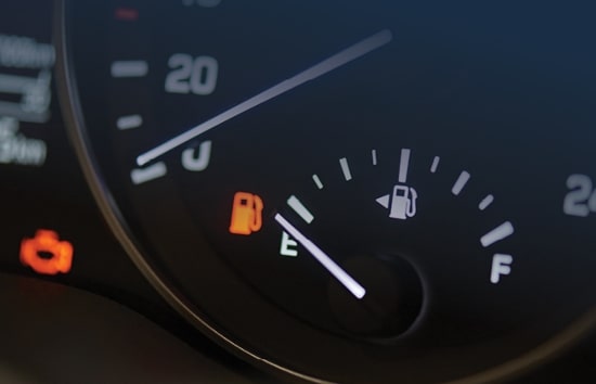 closeup of a fuel gage pointing to “empty” on a car dashboard. The gas pump icon warning light is on.